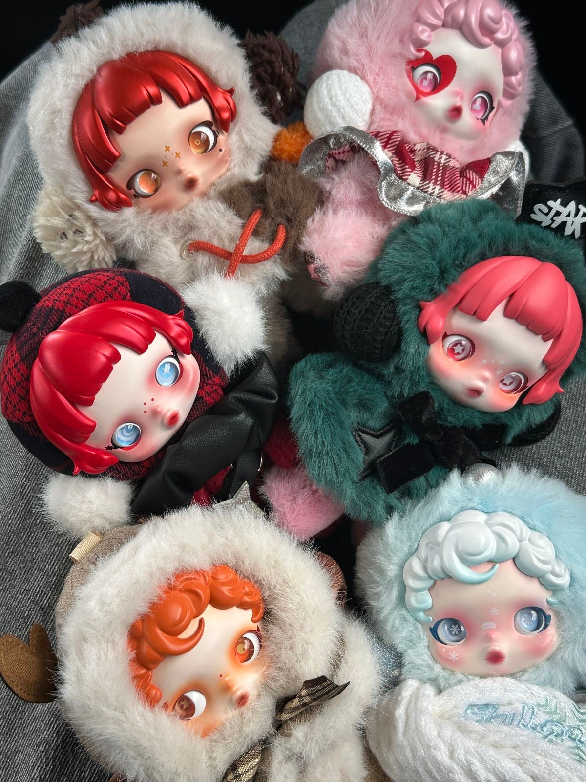 Collection of stylized dolls with various outfits and hairstyles on a textured surface. POP MART POP MART SKULLPANDA Winter Symphony Series Plush blind box — all designs lineup (Wanderer’s Tune, Ode to Cocoa, Song of Snow, Rock On, Rhapsody, Partita, Symphony of Wishes Secret) — Kuwait — سكل باندا ونتر سنفوني- بوب مارت