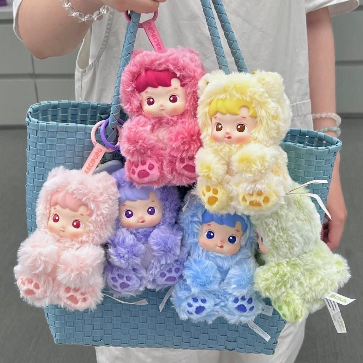 Colorful plush toys in a blue basket held by a person.Pop Mart HACIPUPU Gummy Bear scented plush pendant blind box keychain — Kuwait — بوب مارت