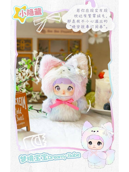 Toy figure with cat ears and a pink bow, sitting on a surface with decorative elements. Nommi V4 Baby Series plush key chain blind box — Dreamy Babe (Secret, pastel lilac/blue) — Kuwait — نومي — Maibo